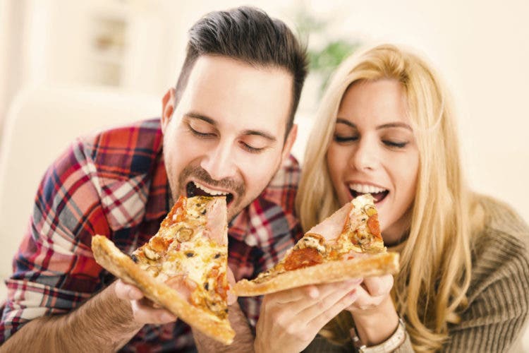 Portrait of an happy couple.They are laughing and eating pizza and having a great time.