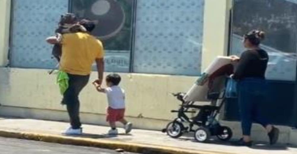 Lleva a su perro pitbull en sus brazos como a un bebé mientras su pequeño hijo camina Lleva a su perro pitbull en sus brazos como a un bebé mientras su pequeño hijo camina